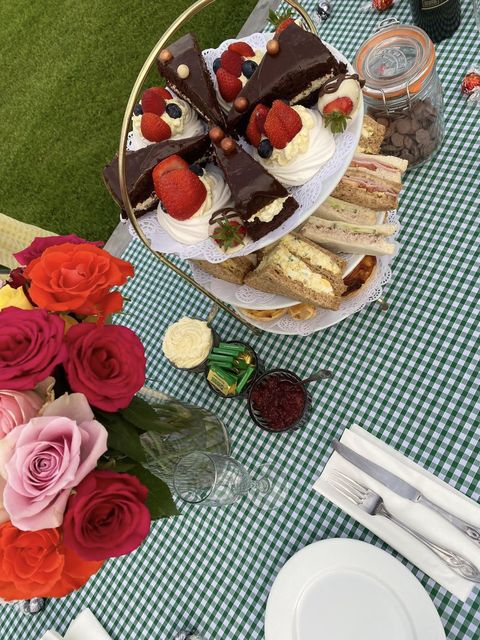 Cake stand of sandwiches and cakes with roses on a gingham table