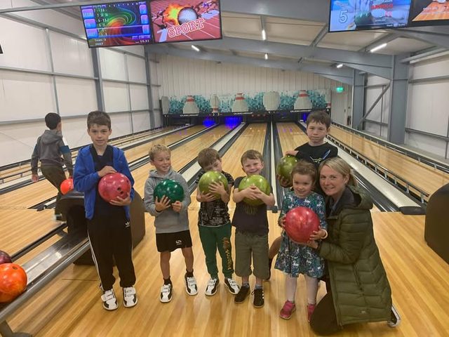 A family holding bowling balls on the lanes