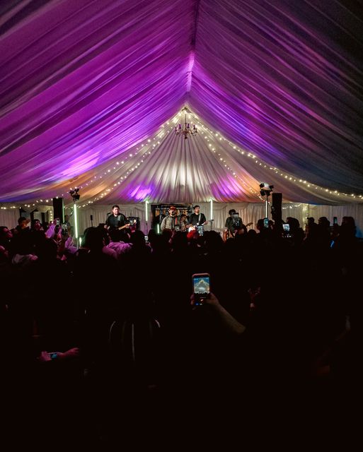 A band on stage in the marquee under purple lights