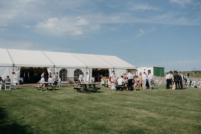Wedding guests at picnic benches on the lawn in front of the marquee