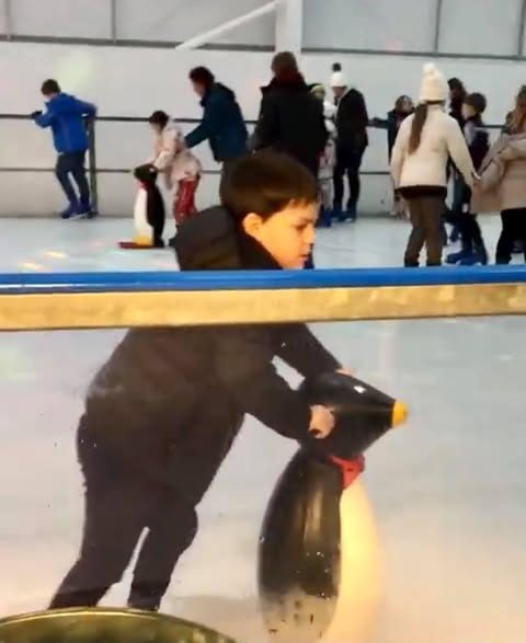 A young skater pushing a penguin skate aid on the ice