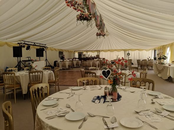 A laid round table beneath flowers hanging from the marquee ceiling
