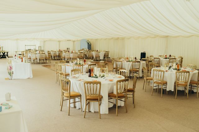 Wide view of the marquee filled with round tables and gold chairs