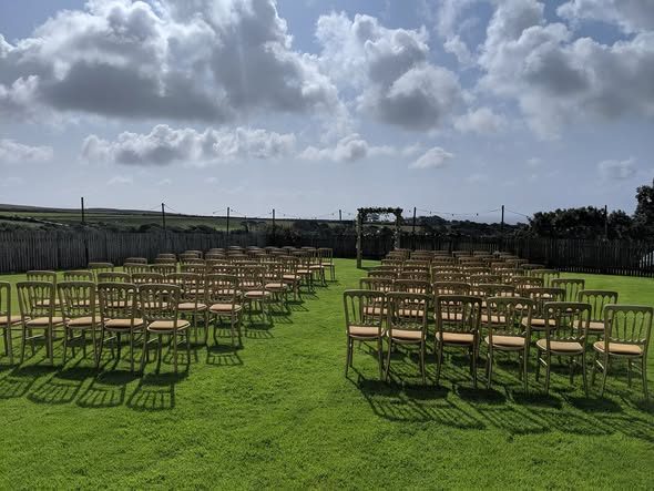 Rows of white chairs set out on the lawn with an arch at the front