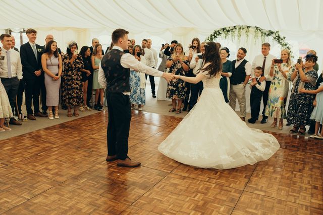 Bride and groom dancing on the wooden dance floor surrounded by guests in the marquee