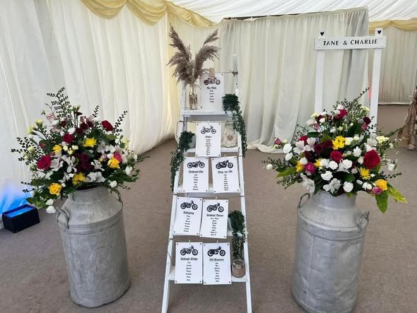 Seating plan on a ladder between two milk churns full of flowers