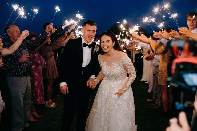 Bride and groom walking through a tunnel of guests holding sparklers at night