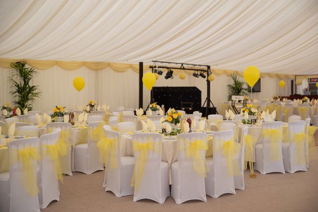 Marquee laid with white chair covers, yellow sashes and yellow balloons